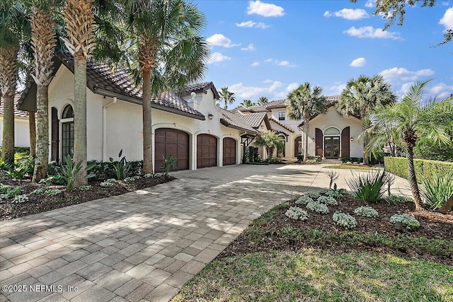 mediterranean / spanish-style house featuring a garage, decorative driveway, a tiled roof, and stucco siding