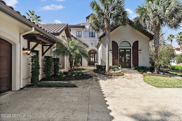 mediterranean / spanish-style home featuring stucco siding, a tiled roof, and french doors