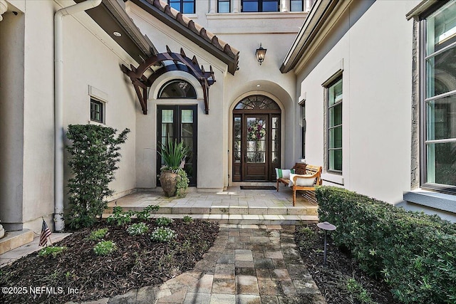 view of exterior entry featuring covered porch, a tile roof, and stucco siding