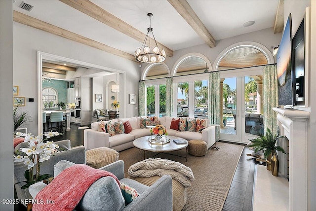 living area featuring an inviting chandelier, beam ceiling, visible vents, and wood finished floors