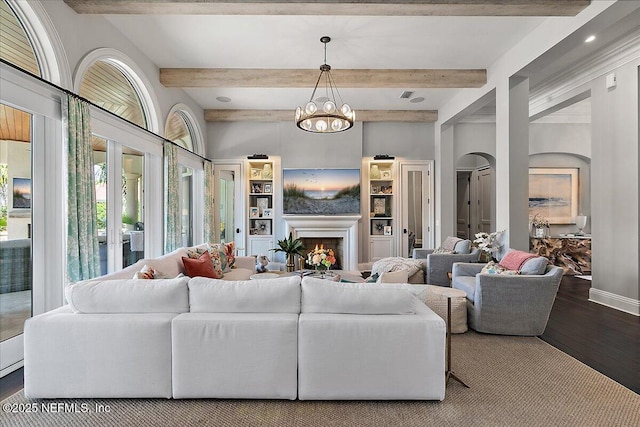 living area featuring beam ceiling, wood finished floors, a chandelier, a lit fireplace, and baseboards