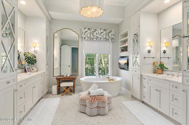 full bathroom with a sink, a freestanding tub, two vanities, and baseboards