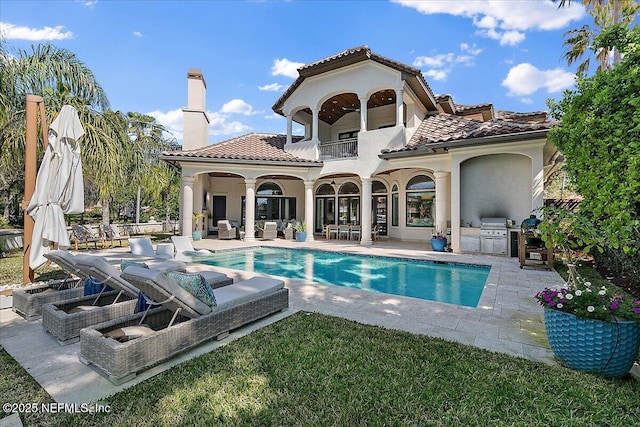 rear view of house featuring a patio, a balcony, a chimney, a tiled roof, and an outdoor living space