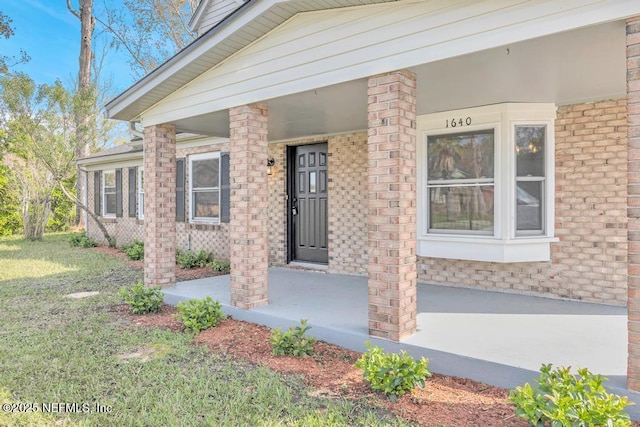 doorway to property with a yard, brick siding, and a porch