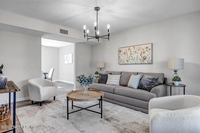 living area with a textured ceiling, a notable chandelier, wood finished floors, visible vents, and baseboards