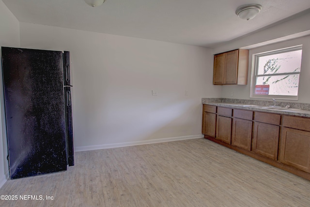 kitchen with baseboards, brown cabinets, freestanding refrigerator, light wood-style floors, and a sink