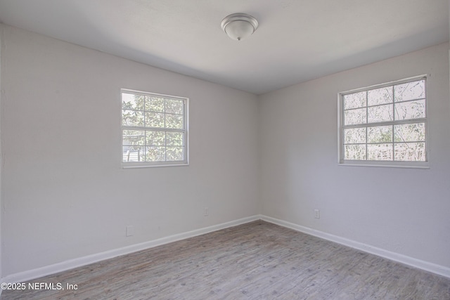 unfurnished room with baseboards, a wealth of natural light, and wood finished floors