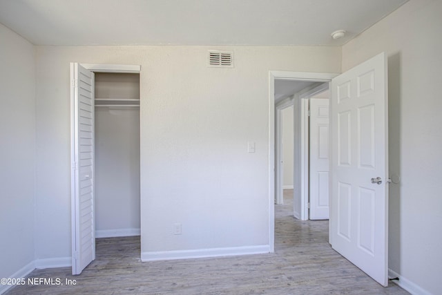 unfurnished bedroom with baseboards, a closet, visible vents, and wood finished floors