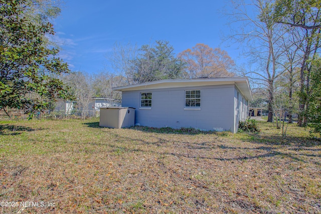 rear view of house with a yard, concrete block siding, and fence