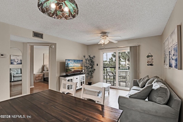 living area with a ceiling fan, a textured ceiling, visible vents, and wood finished floors