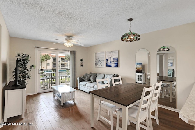 dining room with a ceiling fan, arched walkways, a textured ceiling, and wood finished floors