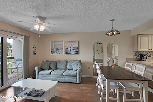 living area with arched walkways, a textured ceiling, wood finished floors, baseboards, and ceiling fan with notable chandelier