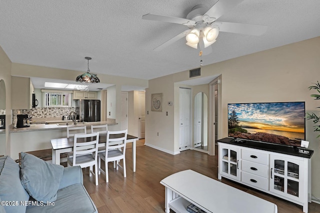 living area with a textured ceiling, wood finished floors, visible vents, and a ceiling fan