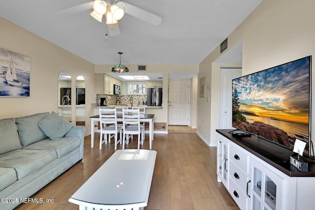 living room featuring a ceiling fan, visible vents, a textured ceiling, and wood finished floors