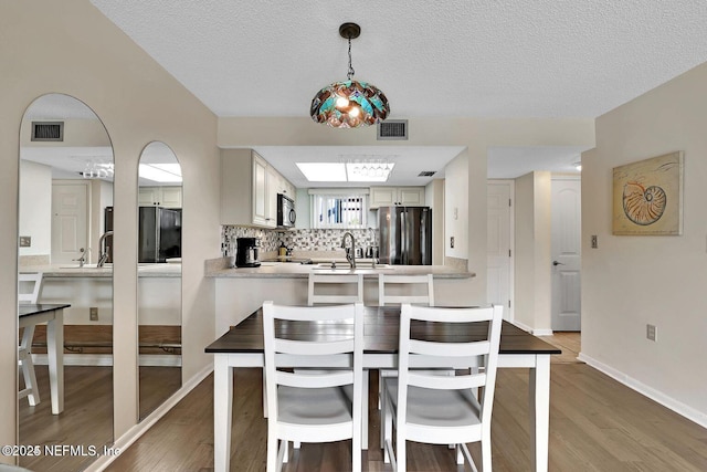 dining space with a textured ceiling, light wood-type flooring, visible vents, and baseboards