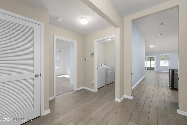 hall featuring washer and dryer, wood finished floors, baseboards, and a textured ceiling