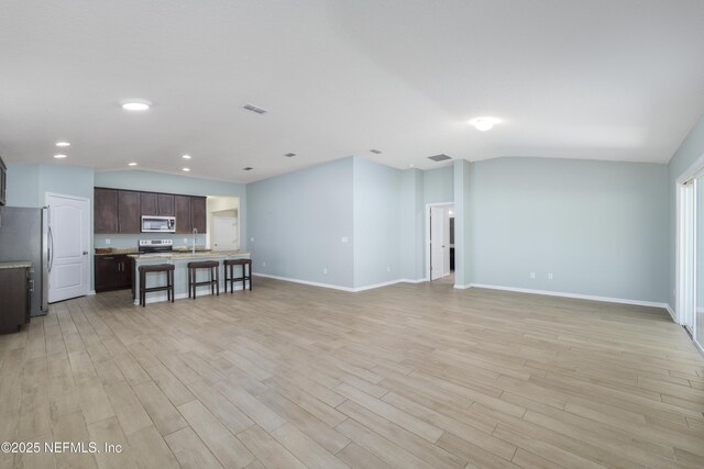 living area featuring visible vents, lofted ceiling, light wood-style floors, and baseboards