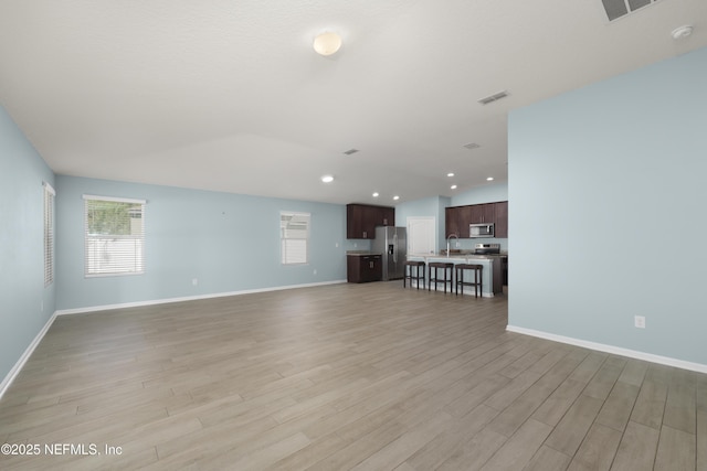 unfurnished living room featuring light wood finished floors, visible vents, baseboards, and a sink