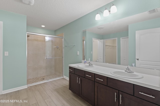 bathroom featuring double vanity, a shower stall, a textured ceiling, and a sink