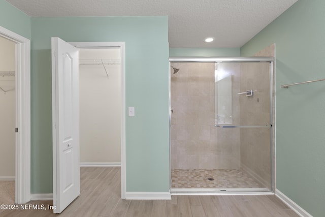 bathroom featuring a walk in closet, a textured ceiling, wood finished floors, a shower stall, and baseboards