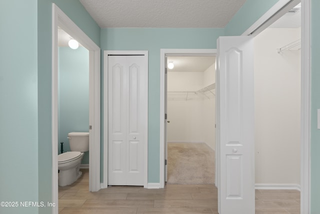 bathroom with baseboards, a textured ceiling, toilet, and wood finish floors