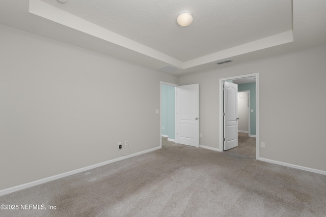 unfurnished bedroom featuring visible vents, baseboards, a tray ceiling, carpet flooring, and a textured ceiling