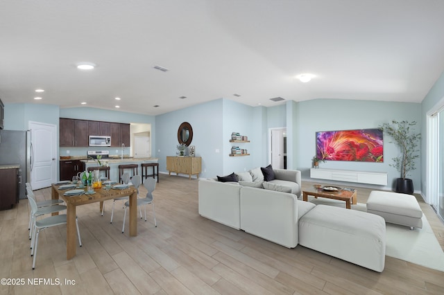 living room with visible vents, recessed lighting, light wood-style floors, and vaulted ceiling