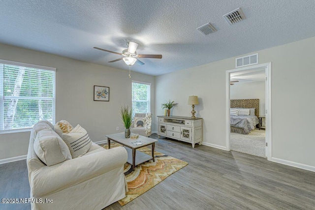 living area with baseboards, wood finished floors, visible vents, and a ceiling fan