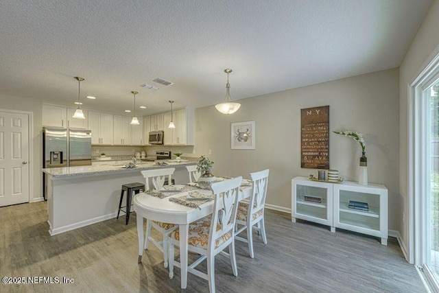 dining area featuring light wood-style flooring, visible vents, baseboards, and a textured ceiling