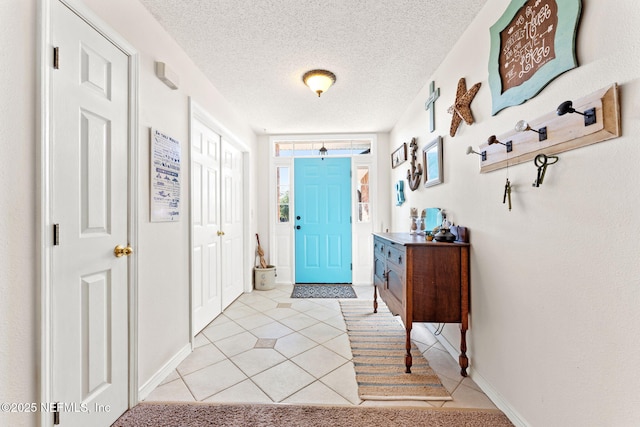 foyer featuring a textured ceiling, light tile patterned floors, and baseboards