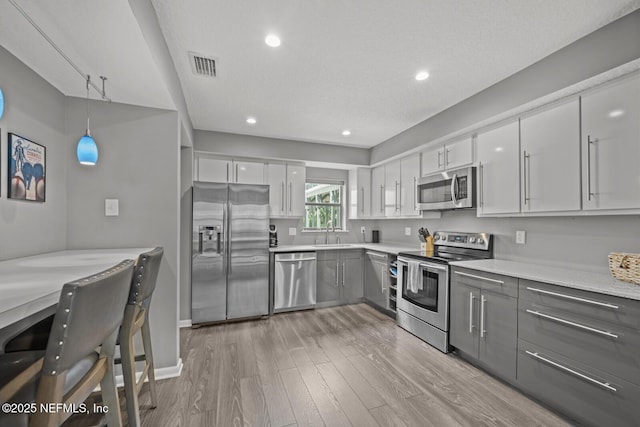 kitchen featuring gray cabinets, visible vents, appliances with stainless steel finishes, light wood-style floors, and a sink