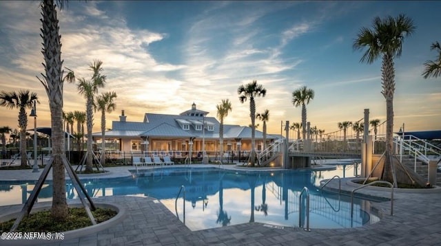 pool at dusk featuring fence and a community pool