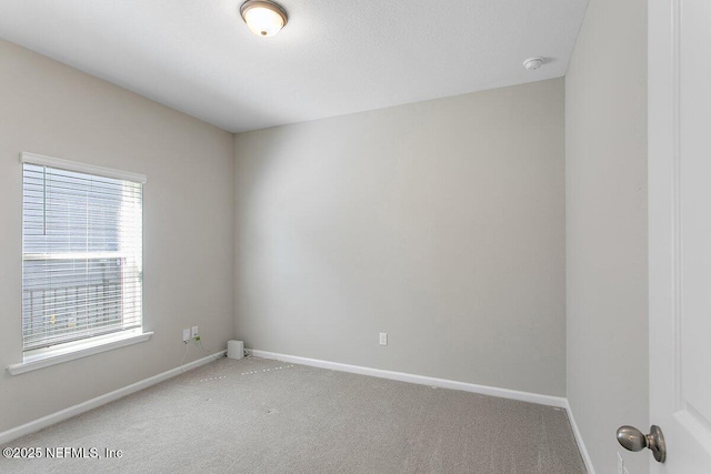 spare room featuring light carpet and baseboards