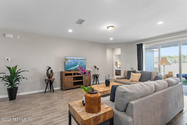 living area featuring wood tiled floor, visible vents, a textured ceiling, and baseboards