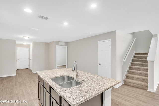 kitchen with a kitchen island with sink, a sink, visible vents, baseboards, and light wood-style floors