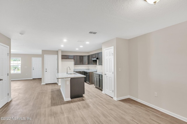 kitchen with light wood finished floors, a sink, a center island with sink, and baseboards