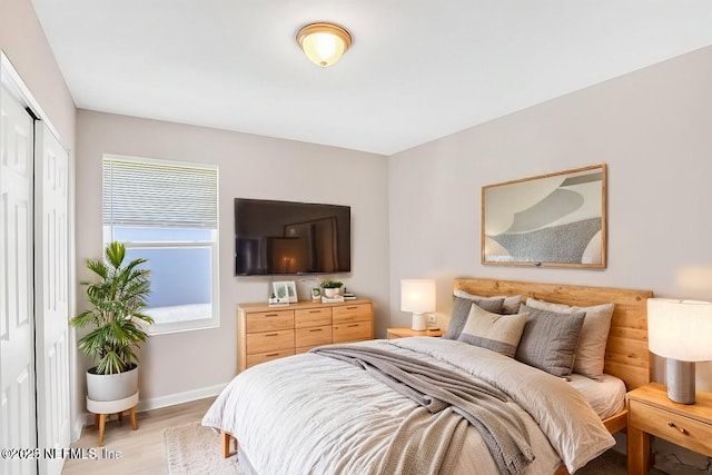 bedroom with a closet, light wood-type flooring, and baseboards