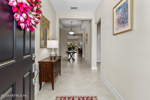 foyer entrance featuring a tray ceiling, visible vents, baseboards, and light tile patterned floors