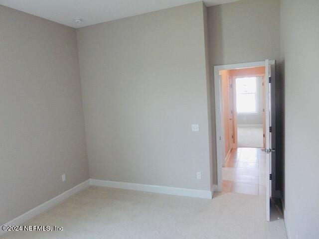 spare room featuring light colored carpet and baseboards