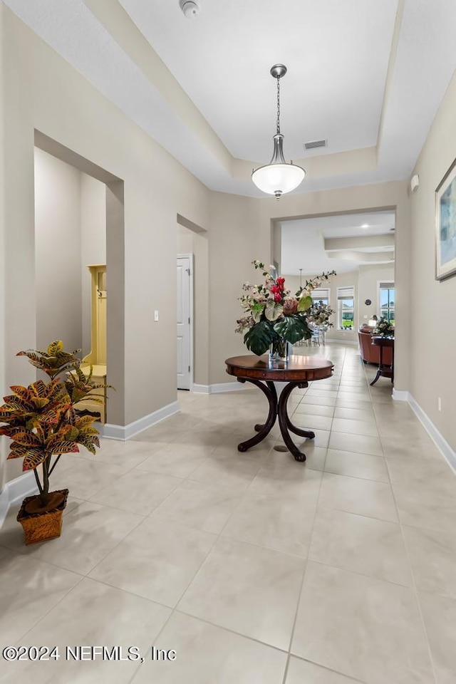 hall featuring light tile patterned floors, a raised ceiling, visible vents, and baseboards