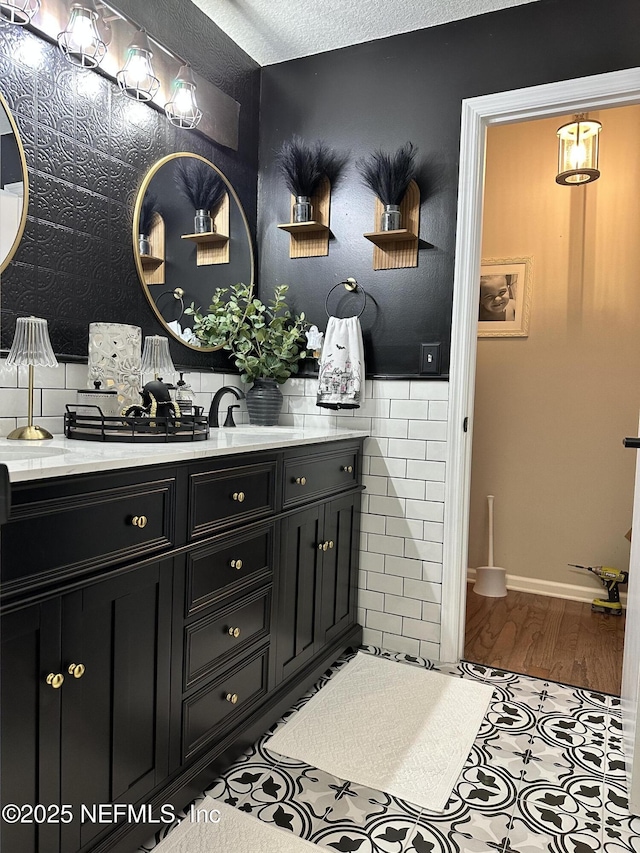 bathroom featuring a textured ceiling, vanity, tile walls, wainscoting, and wallpapered walls