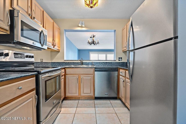 kitchen featuring light tile patterned floors, dark countertops, appliances with stainless steel finishes, a textured ceiling, and a sink