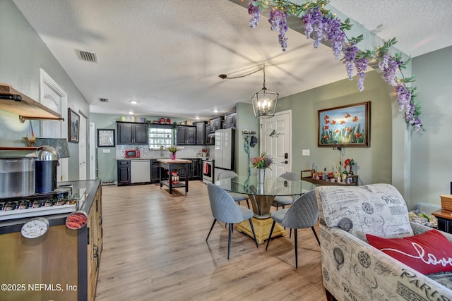 dining room featuring visible vents, light wood-style flooring, and a textured ceiling