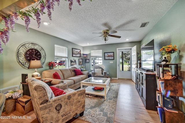 living area with a textured ceiling, recessed lighting, a ceiling fan, visible vents, and light wood-style floors