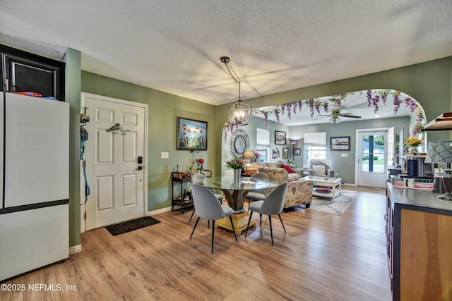 dining space featuring light wood-style floors, baseboards, a textured ceiling, and ceiling fan with notable chandelier