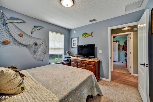 bedroom featuring light colored carpet, visible vents, a textured ceiling, and baseboards