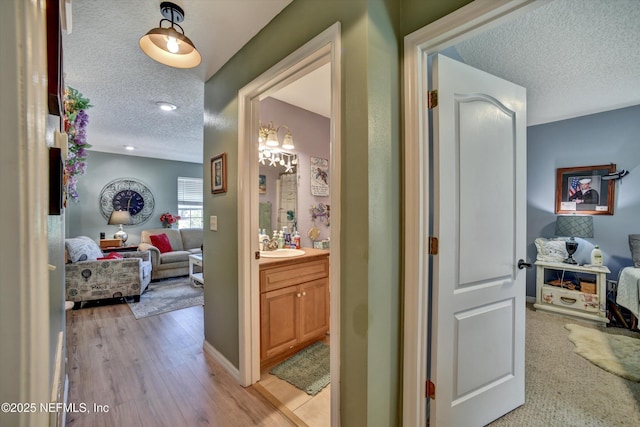 corridor with light wood-style floors, a sink, and a textured ceiling