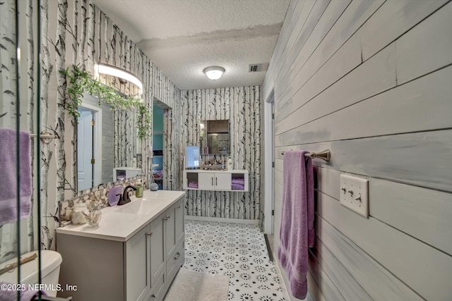 bathroom featuring a textured ceiling, toilet, visible vents, vanity, and wallpapered walls