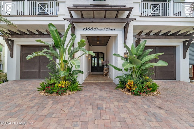 entrance to property featuring an attached garage, a balcony, brick siding, french doors, and decorative driveway