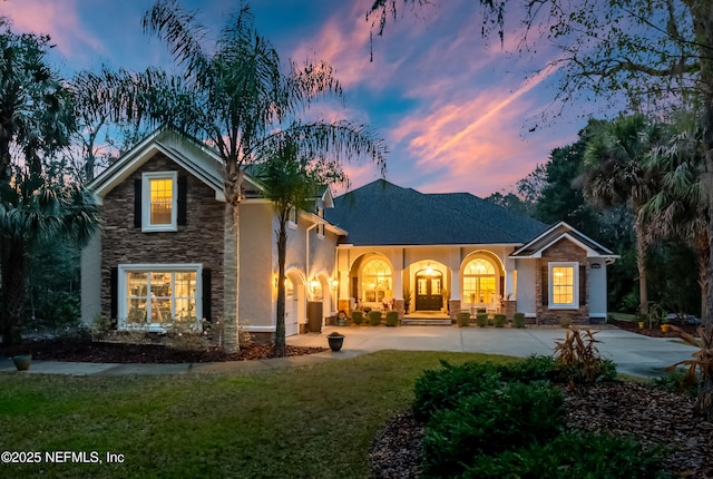 rear view of house with driveway, a yard, stone siding, and stucco siding